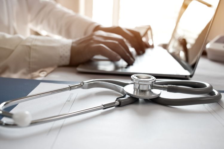 Close-up of a nurse practitioner on a laptop with a stethoscope.