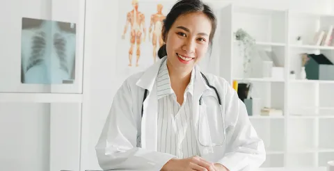 A smiling nurse practitioner stands in an office in front of a chest x-ray.